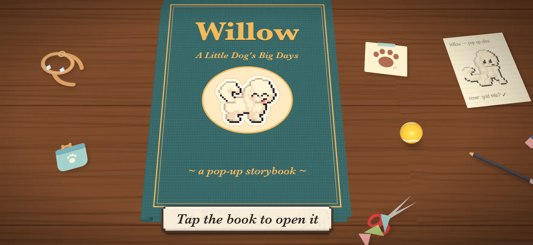 Willow's storybook lying closed on a wooden desk, beside a paw-print card and a tennis ball